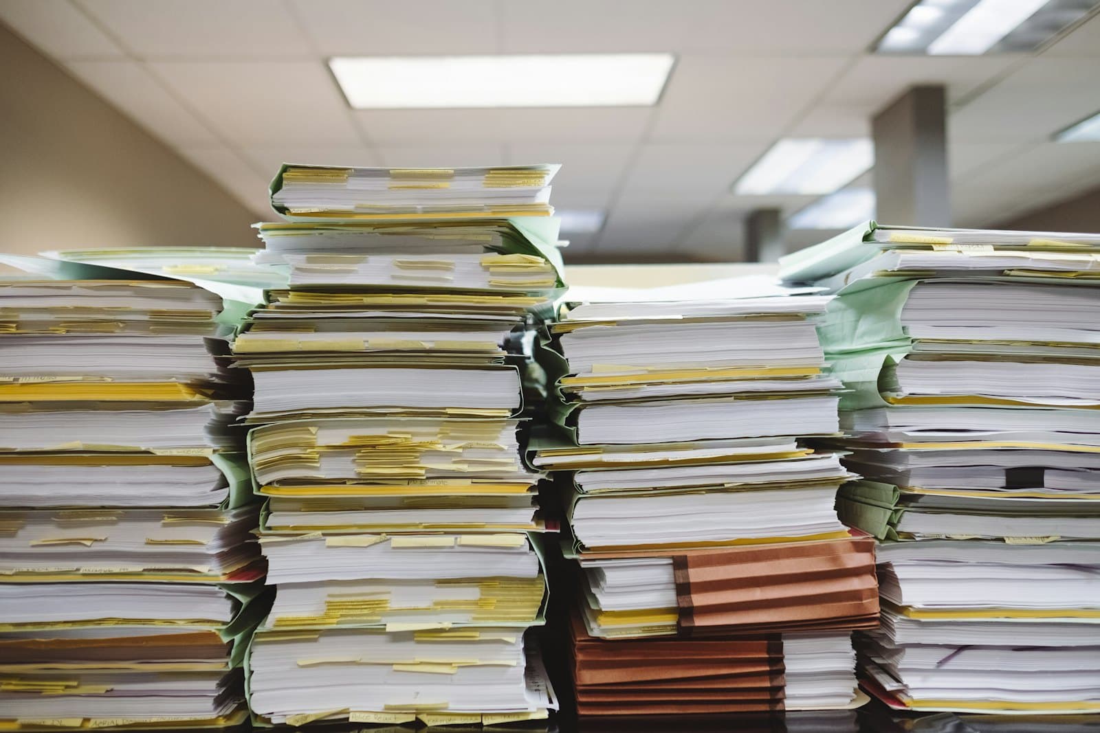 Stacked client file folders and loose paper documents piled on an office desk