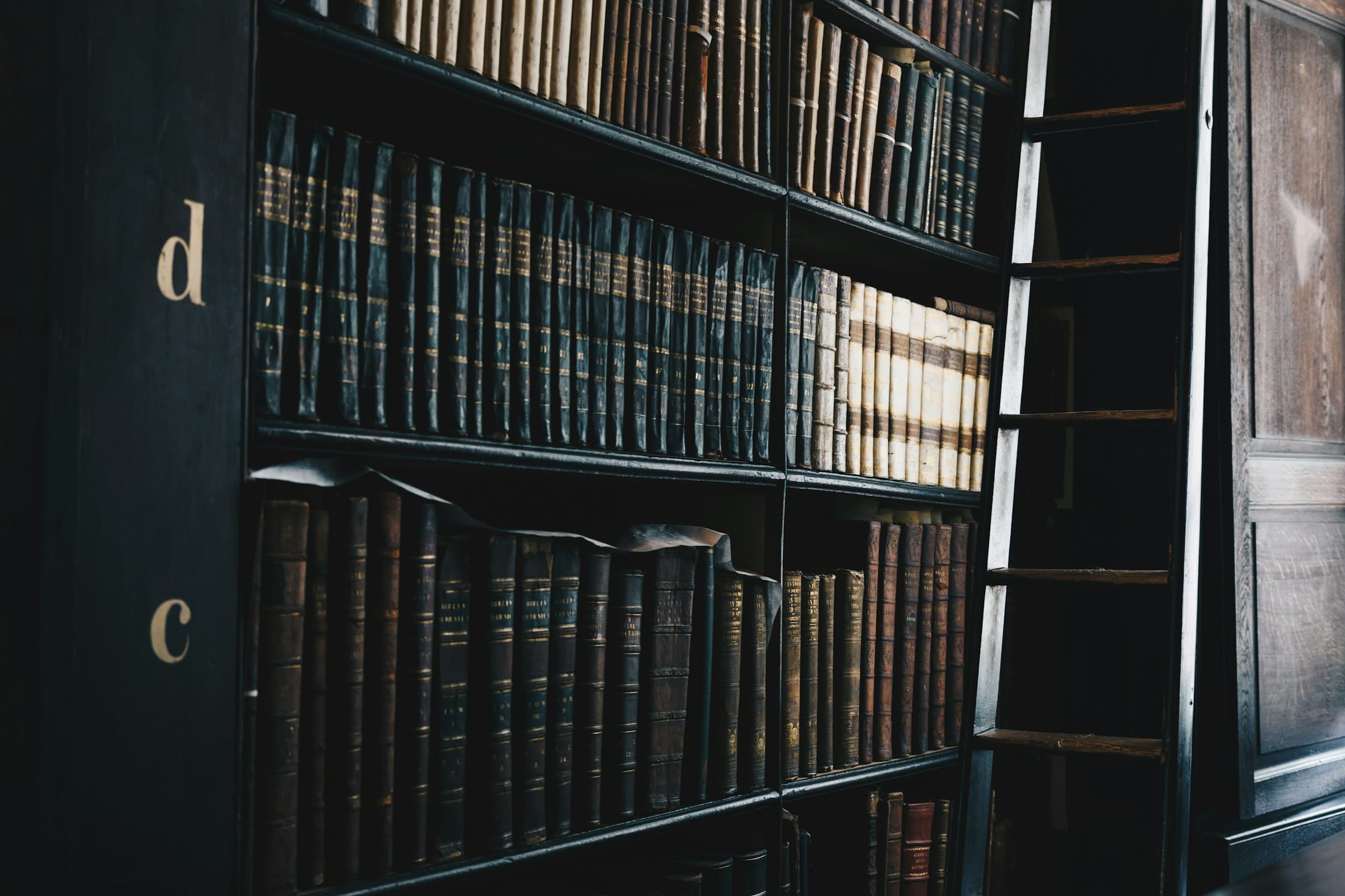 Rows of bound legal volumes on dark wooden shelves in a law library, with a ladder alongside
